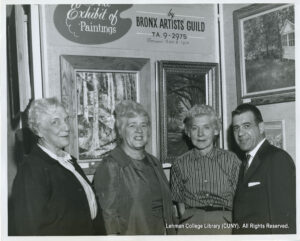 Image of three older women, and one man in a suit. A sign behind them says Bronx Artists Guid, TA 9-2975, between 11am and 1pm, Exhibit of Paintings."