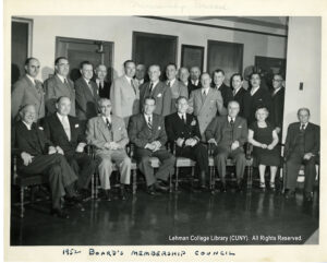 Image of about 30 men in suits, as well as one woman. Half are standing and half are seated.