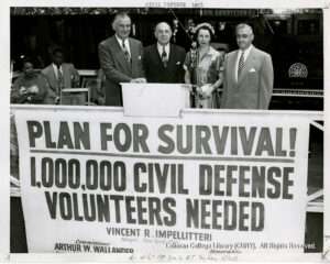 Image of seveal men in suits and one woman in a dress standing at a podium stating "Plan for Survival! 1,000,0000 Civil Defense Volunteers needed (Vincent R. Impellitteri, Mayor)