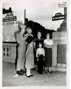Image of a soldier and his family looking at a sign that says "Fordham Road, Grand Concourse, Defense Bond Square."