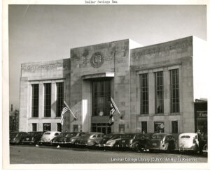 Image of a bank branch decorated with a giant liberty head. Several 1940s or 1950s era cars are parked in front of it.