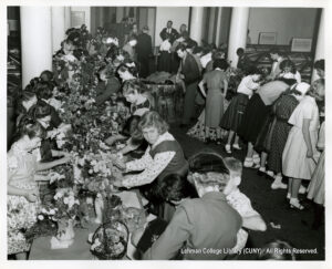 Image of many children, mostly girls, working at tables filled with flowers and vases.