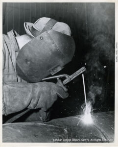 Image of a worker in a welding helmet welding what seems to be a steel pipe.