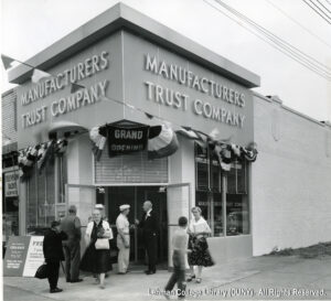 Image of people milling around in front of a branch of Manufacturers Trust Company. The door is open, and a sign says "Open House".