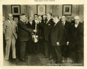 Image of about a dozen men in suits holding a golden shovel and pointing it at the ground.