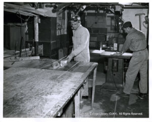 Image of two men in uniforms cutting lumber on table saws.