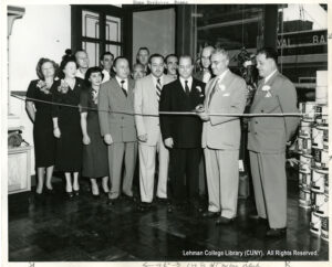 Image of several men in suits and women in dresses stnading in front of a ribbon. Everybody is wearing flower corsages.