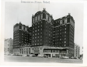 Image of an old timey hotel that is mostly brick facaded. Several cars wait outside.