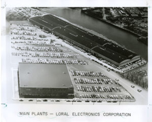 Image of two large factory buildings with large surface parking lots next to a river.