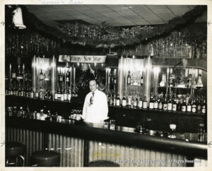 Image of a malebartender, wearing a tie. There is tinsel, bells, and a sign saying "happy new year."