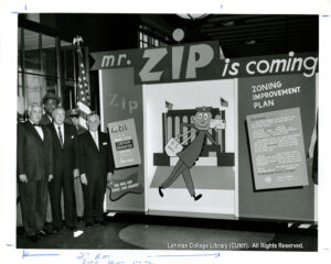 Image of several men in suits, and one in a postal uniform. They are next to a cartoon image of a smiling postman holding a US Mail bag and holding an envelope." He is labeled as "Mr. Zip"