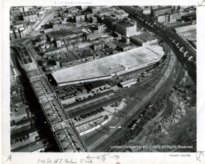 Aerial image of a rail yard with parked cars, buildings, and highways visible.