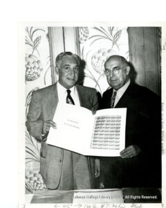 Image of two men in suits holding a book of commemorative stamps.