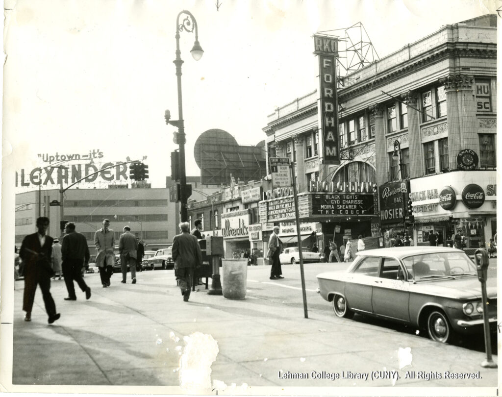 Image of movie theatre, its marquee, and many people and cars. Alexander's store is visible in the background.