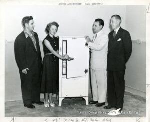 Image of three men in suits. One woman is between them, opening a refrigerator.