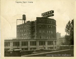 Image of a department store that says "Rogers Department Store." Fire escapes and a water tower are also visible.