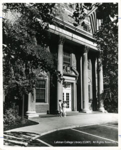 Image of two women in front of a columned building. The building has a sign that says "Barnabas Hospital"