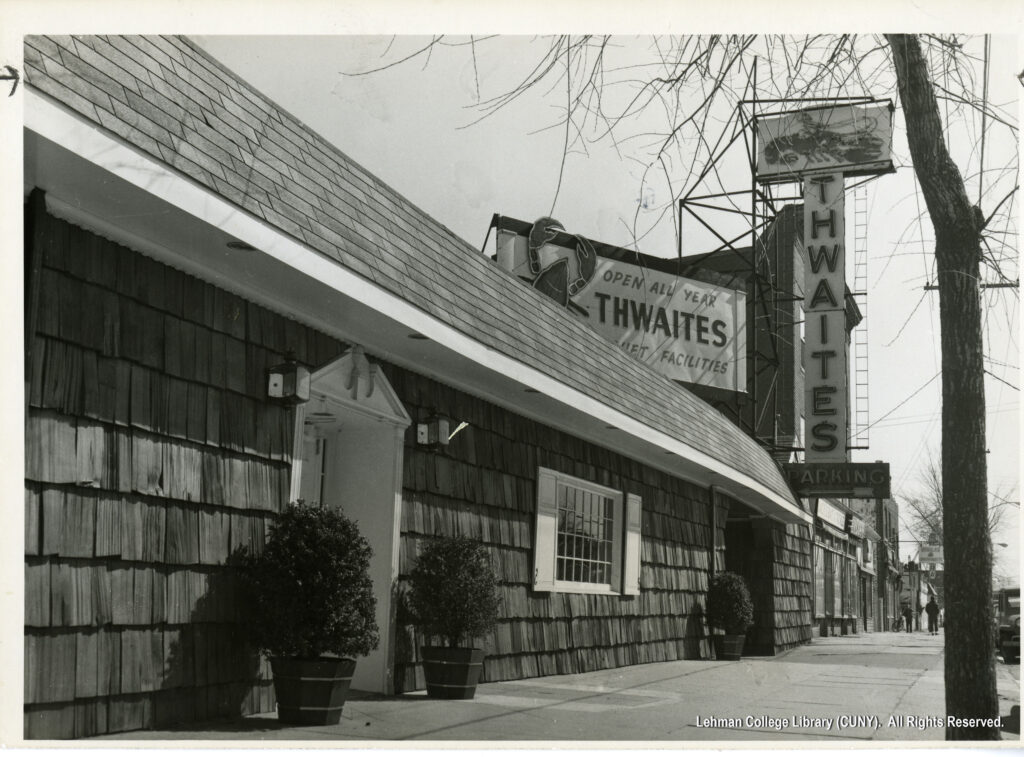 Image of a wood shingled restaurant. A sign proclaims "Thwaits" and says it is open all year. Two signs decorated with oversized lobsters are also visible.