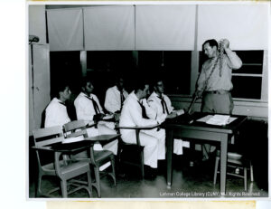 A man holds a grappling hook and appears to be talking to a group of five sailors.