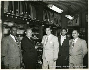 Image of several men and one woman in suits looking at a camera. One man appears to be giving a plaque to another.