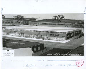Image of a 1 story factory with several buildings. Cars and people are also visible. Image says "Milau Associates"