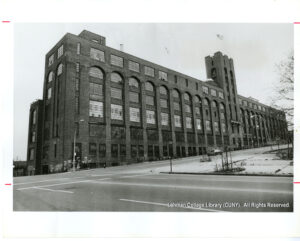 Image of a large factory building on a slanted hill. A car sits in front of it.