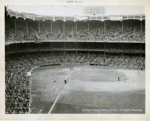Image of the interior of Yankee Stadium showing crowds and a ballgame in progress. A shorstop appears to be throwing a ball toward Third Base