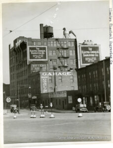 Image of a large building with billboards for Electro-Chemical Engraving Co, Greases Garage, and Washington Stables.