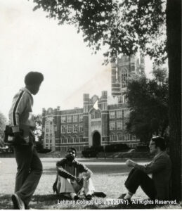 Image of students chatting on the grass at Fordhman University, in front of a collegiate gothic building.