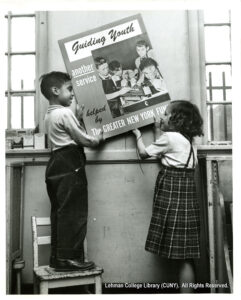 Image of two children, one a standing girl and one a boy standing on a chair, hanging up a sign that says "Guiding Youth - Another service helped by the Greater New York Fund."