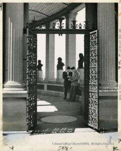 Image of two students reading behind an iron gate and in front of busts of famous Americans.