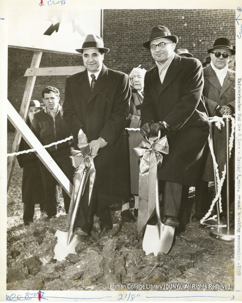 Image of two men with shovels decorated with ribbons putting them into the ground. Several other men look on.