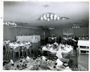 Image of a catering hall with chairs, pitchers of water and flowers on tables.