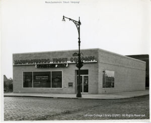 Image of a branch of Manufacturer's Trust Company. There are cobblestone streets and an ornate lamp post visible. Signs for Boston Road and Corsa Ave are also visible.