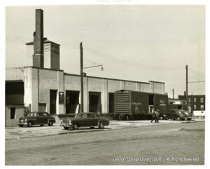 Image of a building with a sign saying "National Plywood". A boxcar appears to be loading and several cars are also present.