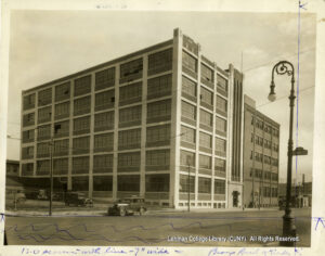 Image of a factory building. Several 1920s-era cars are visible as is an ornate lamp-post attached to a sign saying 14th Street.